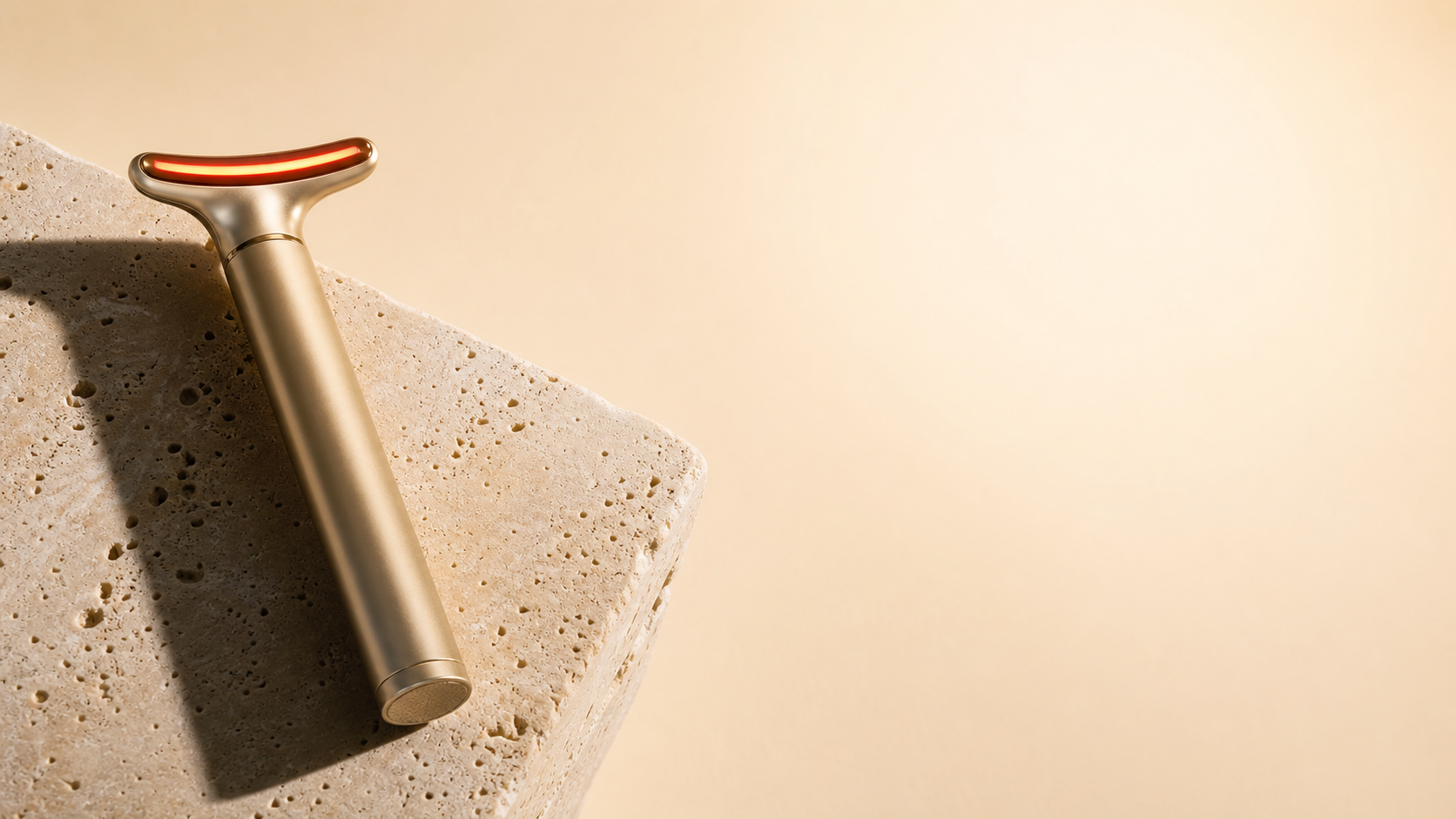 Gold LED skincare wand resting on a travertine stone slab