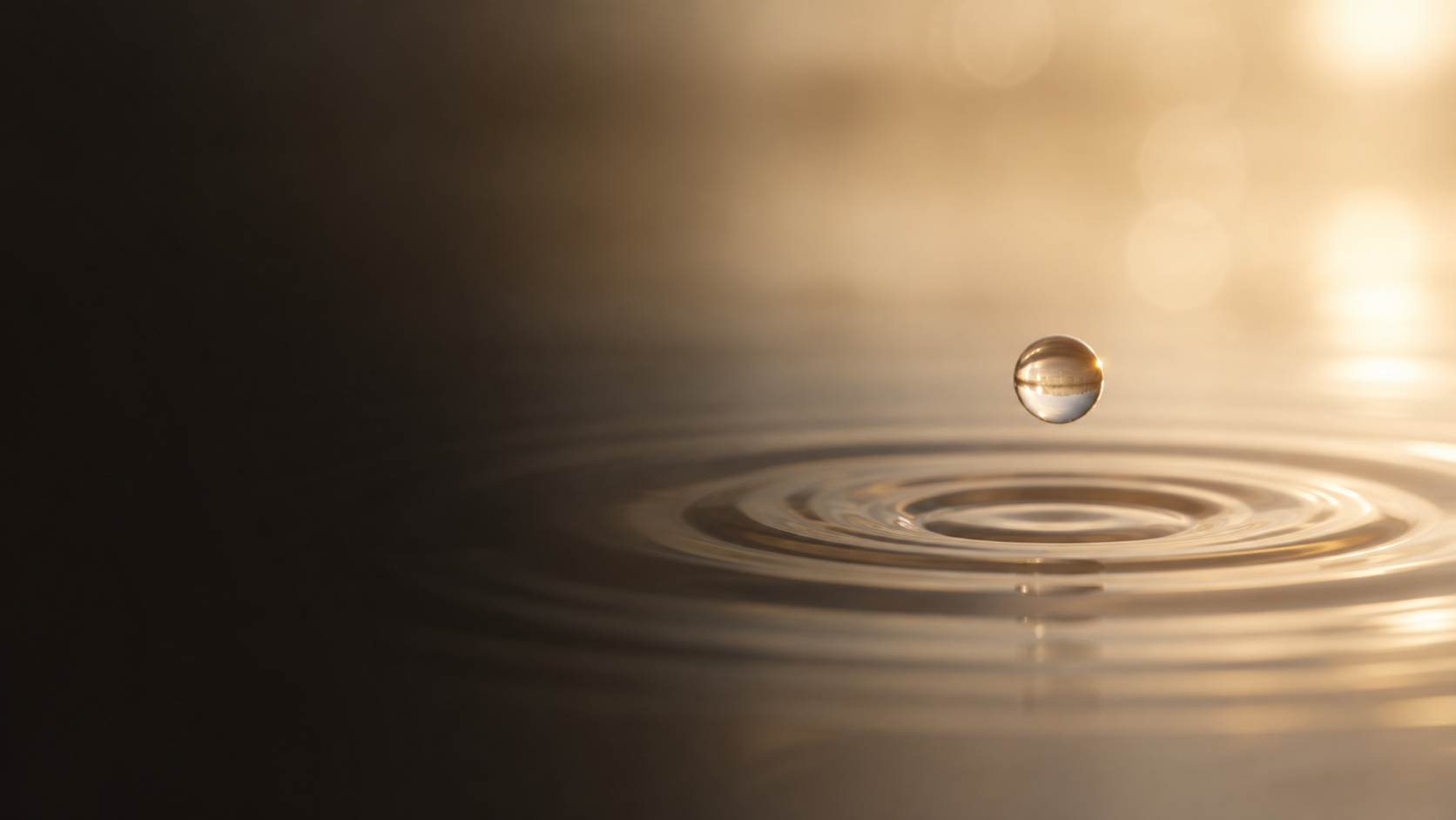 A single water droplet falling onto a calm golden water surface